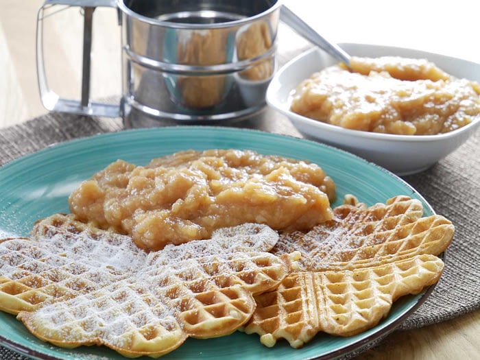 Image of a plate of vanilla-colored Belgian waffles with a generous helping of salted caramel drizzled on top, a spoonful of diced apples and a dollop of cream